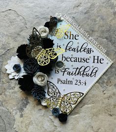 a graduation cap decorated with black and white flowers on top of a stone slab that says she is fearless, because he is faithful