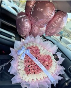 pink and white roses arranged in a heart shaped arrangement with balloons on the back of a car