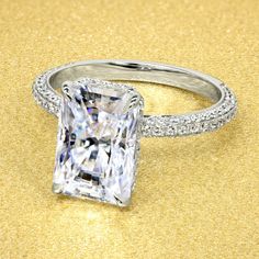 an engagement ring with a princess cut diamond surrounded by pave diamonds on a gold background