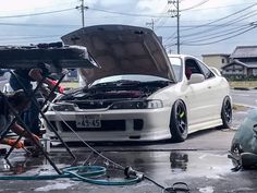 two men working on the hood of a car that is being worked on by another man