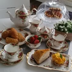 a table topped with plates and cups filled with pastries on top of a white table cloth