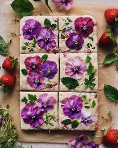 flowers and strawberries laid out on top of a piece of parchment with icing