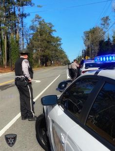 two police officers standing next to each other on the side of the road with their lights on