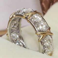 two diamond wedding rings sitting on top of a white cloth covered box with gold trimming