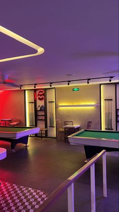 a pool table and ping pong tables in a room with neon lights on the walls