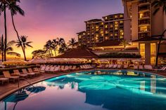 an outdoor swimming pool with chaise lounges and palm trees in the background at sunset