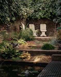 two white chairs sitting on top of a lush green hillside next to a small pond