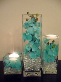 two clear vases with blue flowers and candles on a black countertop next to each other