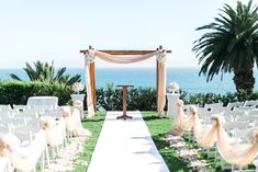 an outdoor ceremony setup with white chairs and flowers on the aisle, overlooking the ocean