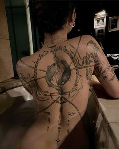 a woman sitting in a bathtub with tattoos on her back