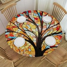 the table is set with plates and cups in front of a stained glass tree design