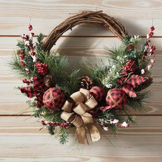 a christmas wreath with pine cones, red and black plaid ornaments and bows on a wooden wall