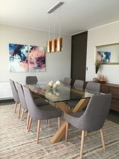 a glass dining table with grey chairs and artwork on the wall in an open living room