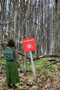 a woman with a backpack is standing in the woods looking at a sign that says manmade