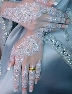 two hands with white lace on them, one holding the other's hand and wearing gold rings