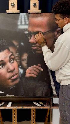 a man standing in front of a large painting with people on it's face