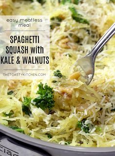 spaghetti with kale and walnuts is being stirred by a fork in a skillet