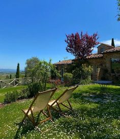 two lawn chairs sitting on top of a lush green field next to a stone building