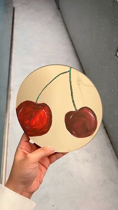 a person holding up a plate with two cherries on the front and back of it