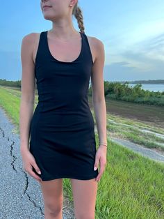 a young woman standing on the side of a road wearing a black dress and sandals