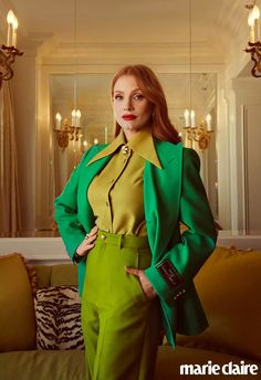 a woman standing in front of a couch wearing a green suit and yellow shirt with her hands on her hips