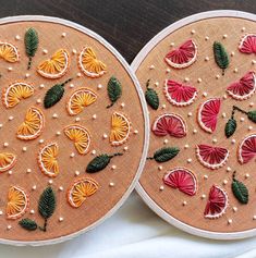 two hand embroidered oranges with leaves and flowers on them, sitting next to each other