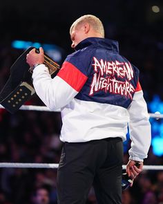 a man in an american nightmares jacket standing next to a wrestling ring with his hand on his hip