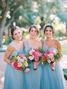 three bridesmaids in blue dresses with pink and green bouquets smiling at the camera