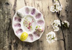 an easter egg tray with painted eggs on it next to some white flowers and branches