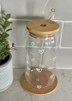 a glass jar with wooden lid sitting on a counter next to a potted plant