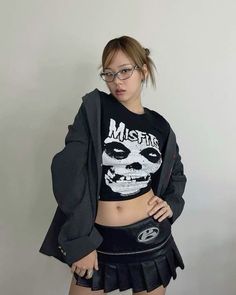 a girl with glasses and a skull shirt is posing for the camera while wearing a skirt