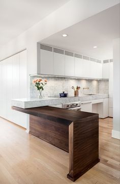 a kitchen with white cabinets and wood flooring, an island in the middle is surrounded by marble counter tops