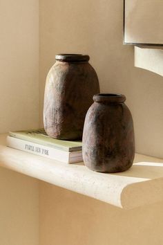 two brown vases sitting on top of a white shelf next to a bookshelf