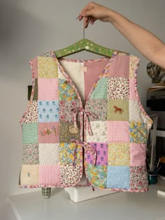 a woman's hand holding onto a patchwork vest hanging on a clothes rack