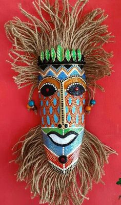 a colorful mask is hanging on the wall with long grass in it's mouth