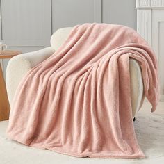 a pink blanket sitting on top of a white chair next to a wooden side table