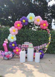 an outdoor birthday party with balloons and decorations on the side walk in front of a hedge