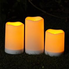 three lit candles sitting in the grass at night