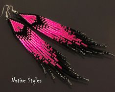 pink and black beaded earrings with long fringes hanging from hooks on dark background