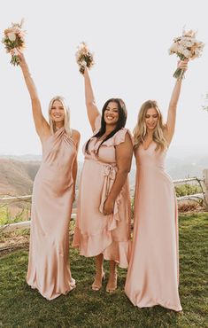 three bridesmaids in pink dresses holding bouquets and posing for the camera with their arms up