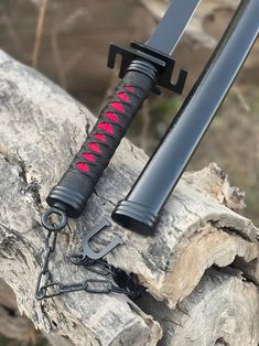 a black and red knife sitting on top of a piece of wood next to a tree