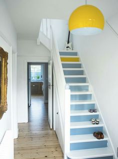 there is a hallway with blue and white striped stairs next to a yellow framed mirror