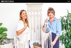 two women standing next to each other in front of a macrame wall hanging