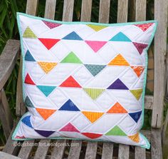 a colorful quilted pillow sitting on top of a wooden bench next to a plant