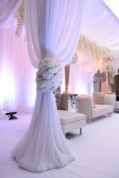 a white wedding ceremony setup with flowers and draping on the back of it