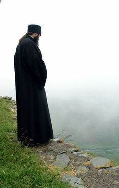 a man standing on top of a grass covered hill next to a stone wall in the fog