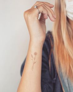 a woman with a small tattoo on her arm holding a flower in her left hand