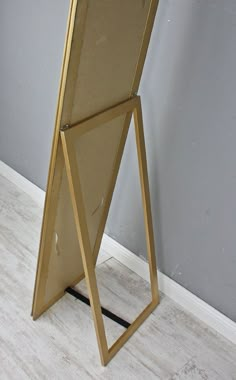 a gold framed mirror sitting on top of a wooden floor next to a gray wall