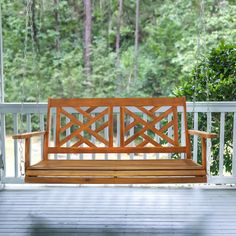 a wooden bench sitting on top of a porch next to a tree filled forest with lots of green leaves