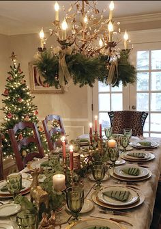 a dining room table set for christmas dinner with candles on the plates and place settings